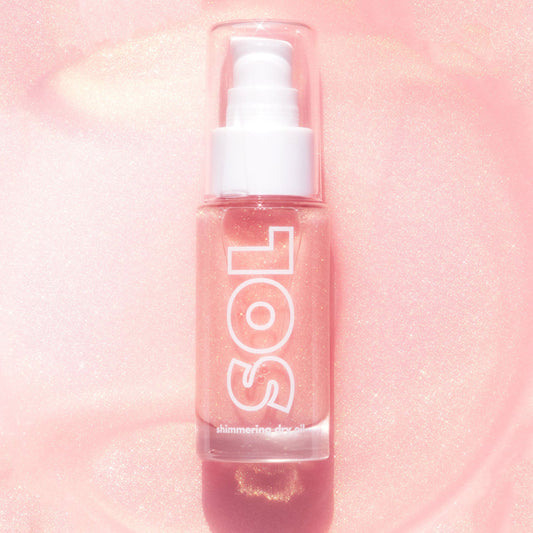 ColourPop SOL Shimmering Dry Oil in Pink Champagne stands upright with a pump and clear cap, showcasing rose-pink, gold-flecked oil in a glass bottle labeled SOL against a luminous pink glitter background.