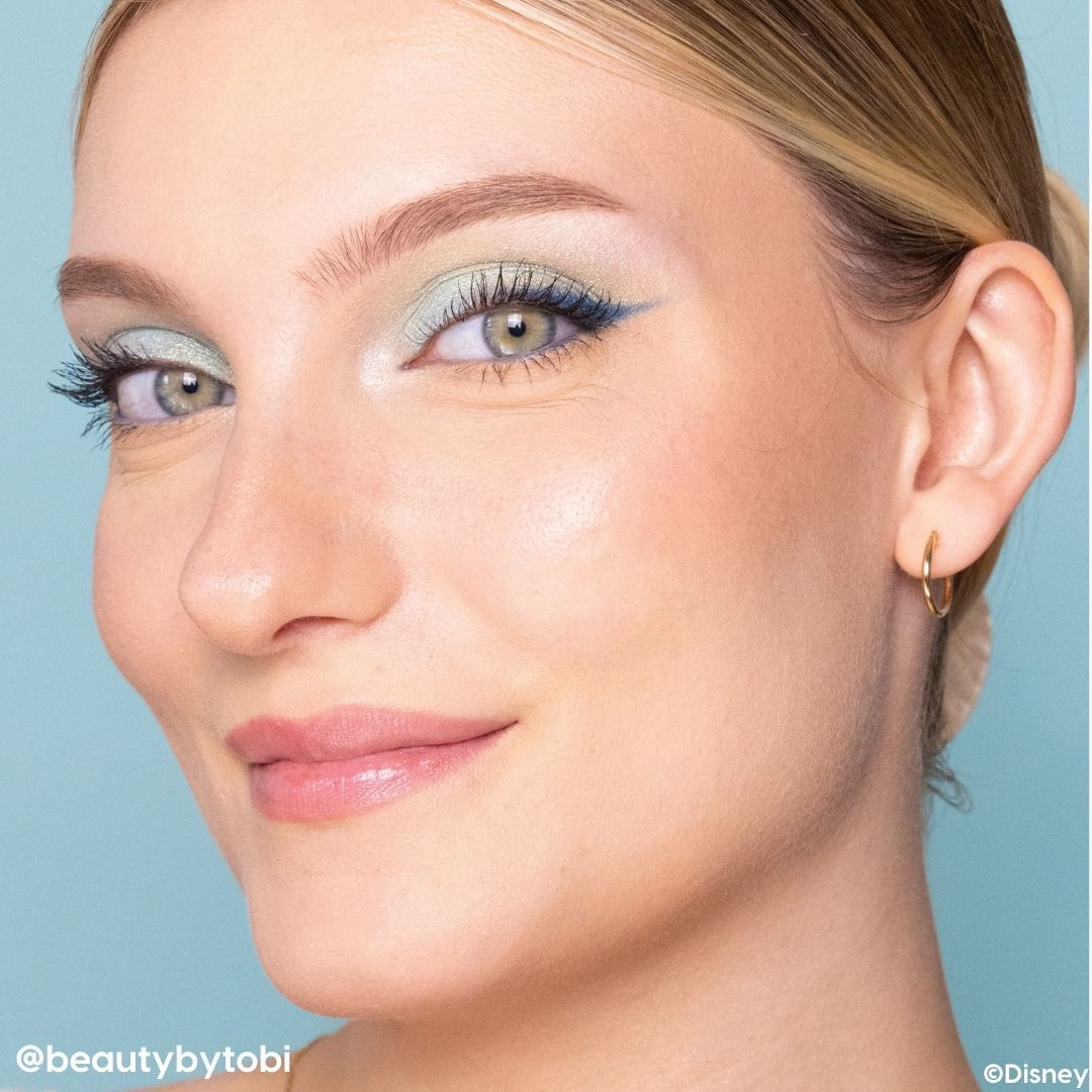 Enchanted Rose lip mask delivering a glossy, hydrated pink sheen on lips, shown on a close-up model with pastel teal winged eye makeup against a light blue background; a nourishing ColourPop Lip Mask for soft, smooth lips.
